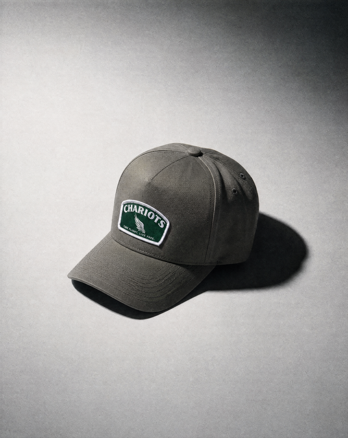 A GREY baseball cap with a green and white 'CHARIOT'S' logo patch on the front, photographed on a gray background with a soft shadow.