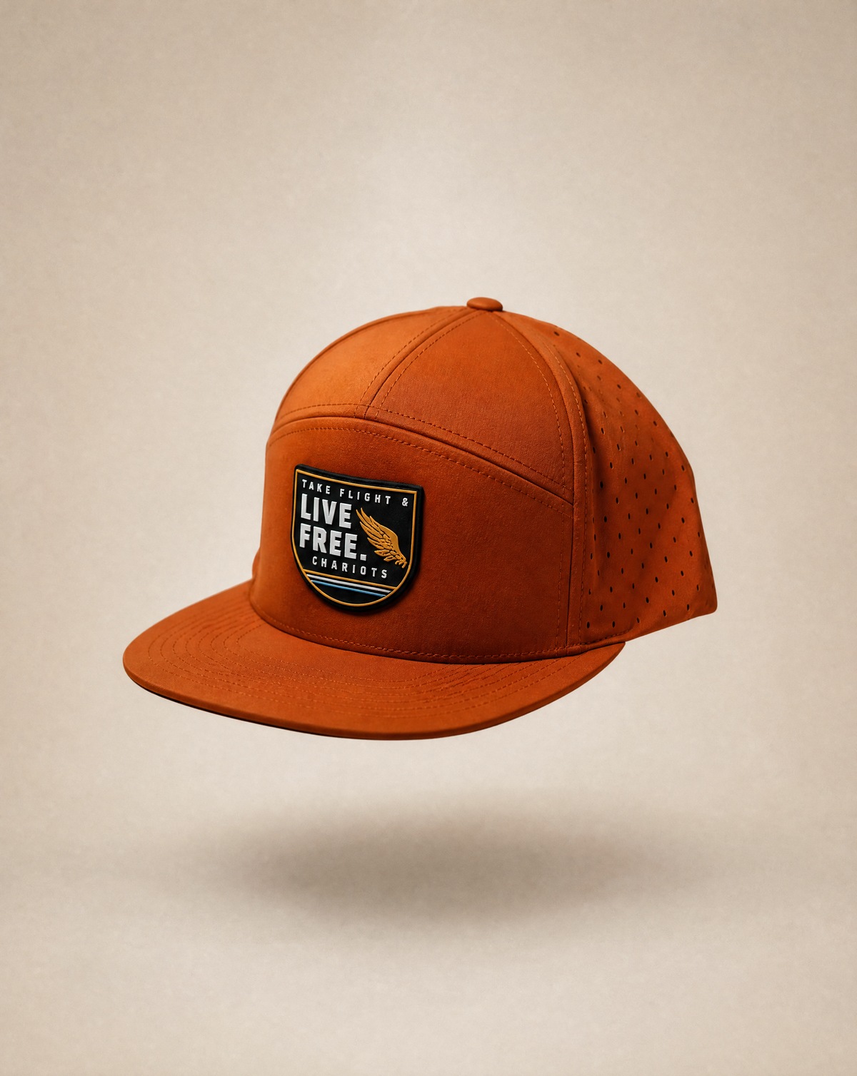 An orange 5-panel baseball cap with a structured flat brim, perforated side panels, and a front patch reading 'TAKE FLIGHT. LIVE FREE. CHARIOTS.
