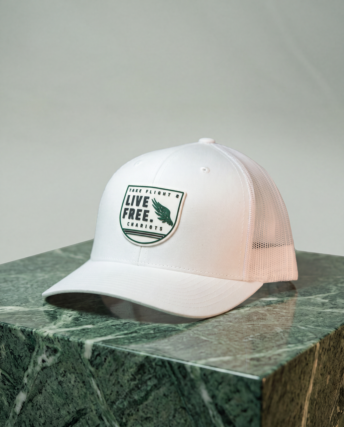 A white trucker-style baseball cap with a green and black 'Live Free. Take Flight.