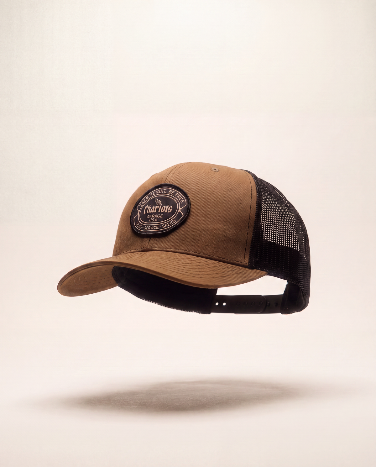 A brown and black trucker cap with a circular embroidered patch on the front, shown floating against a light beige background.