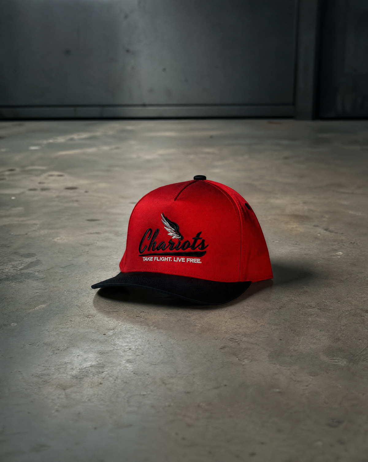 A red and black snapback cap with 'Cheroiots' embroidered on the front, resting on a concrete floor against a dark gray wall.