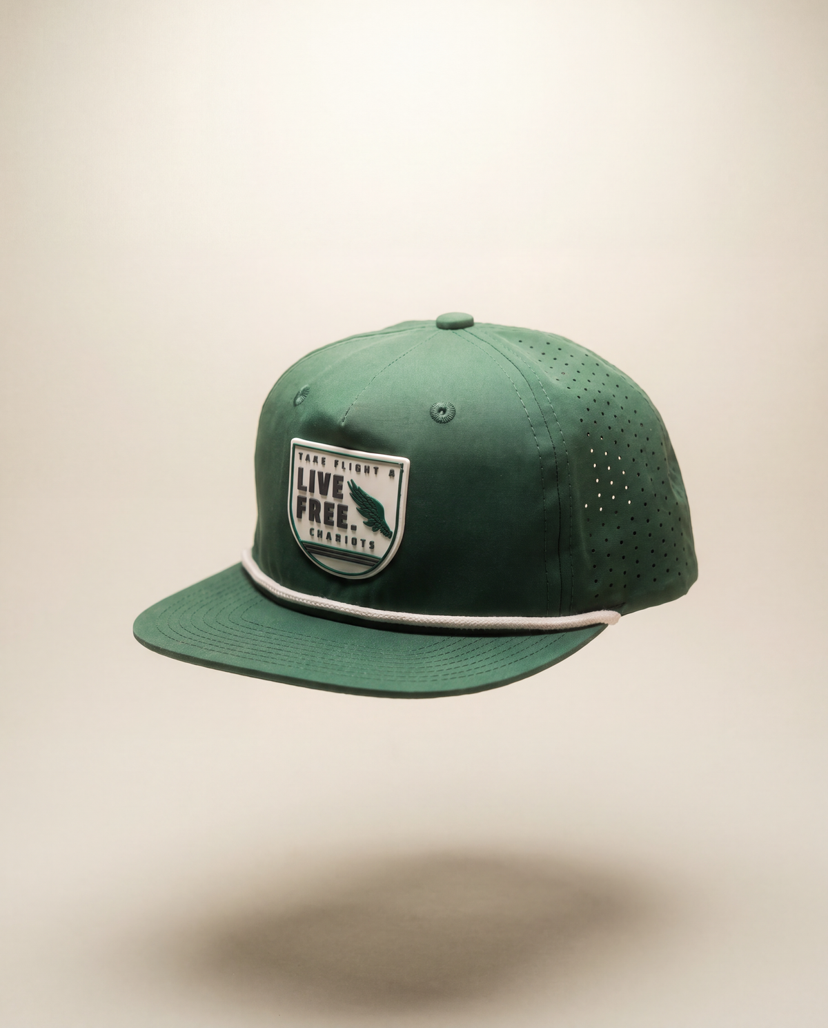 A green flat-brim baseball cap with a white embroidered patch on the front that reads 'TAKE FLIGHT LIVE FREE CHARIOTS' with a rifle graphic, shown against a plain beige background.