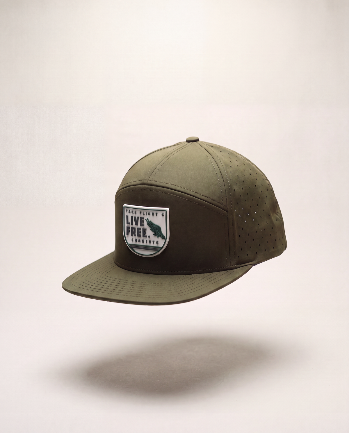 An olive green flat-brim cap with a front patch reading 'TAKE FLIGHT LIVE FREE CHARIOTS' and a fish silhouette, shown floating against a light beige background.